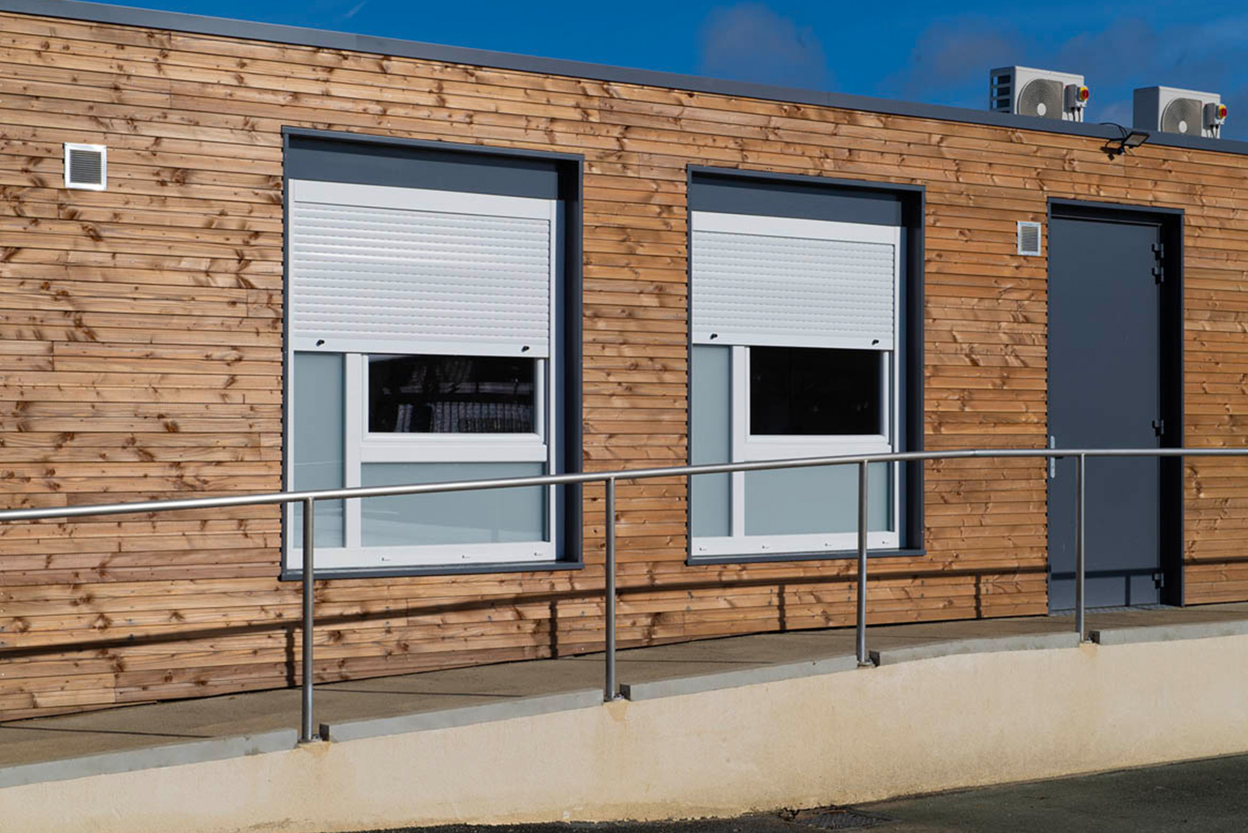façade en bois sur bâtiment modulaire avec rampe, double fenêtre et climatisation algeco