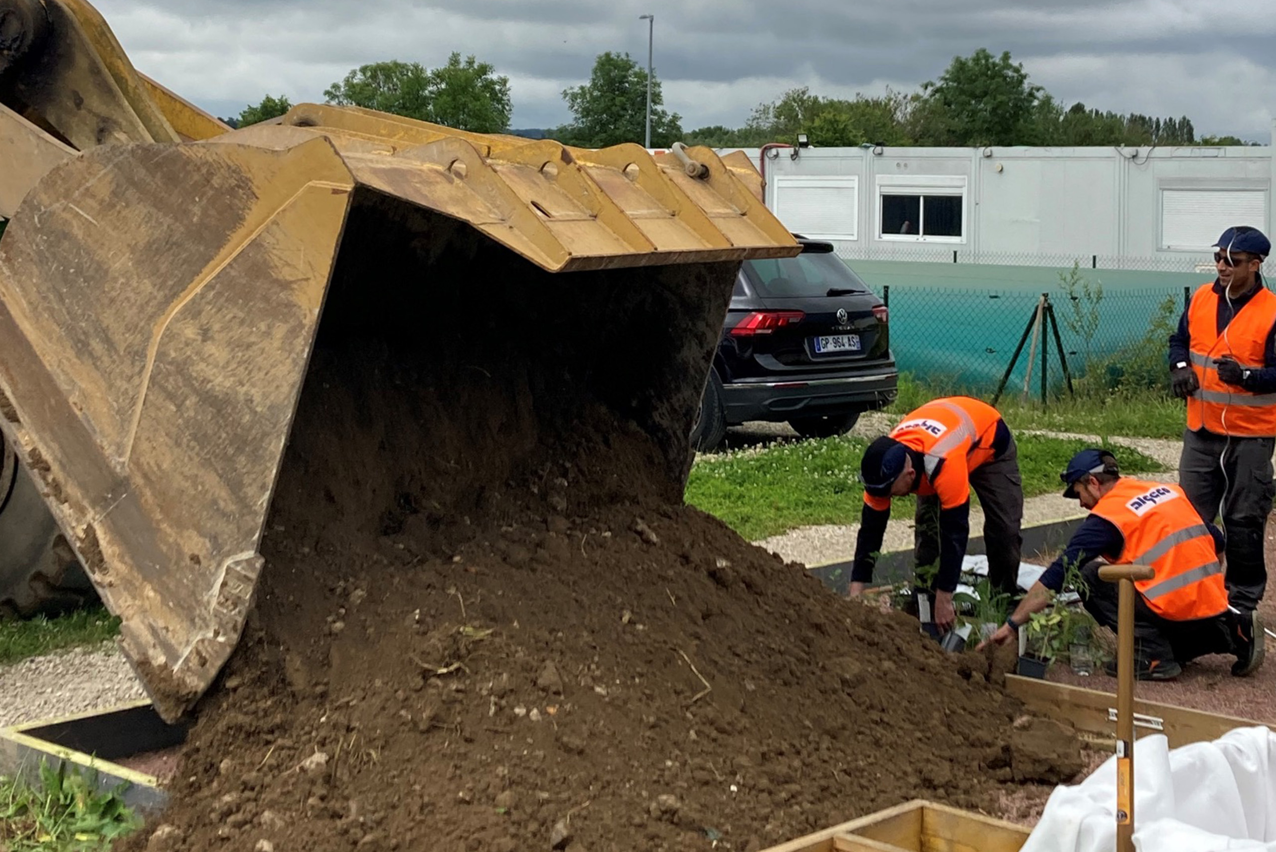 ouvriers d’Algeco en action déversant de la terre grâce à une grande pelle mécanique