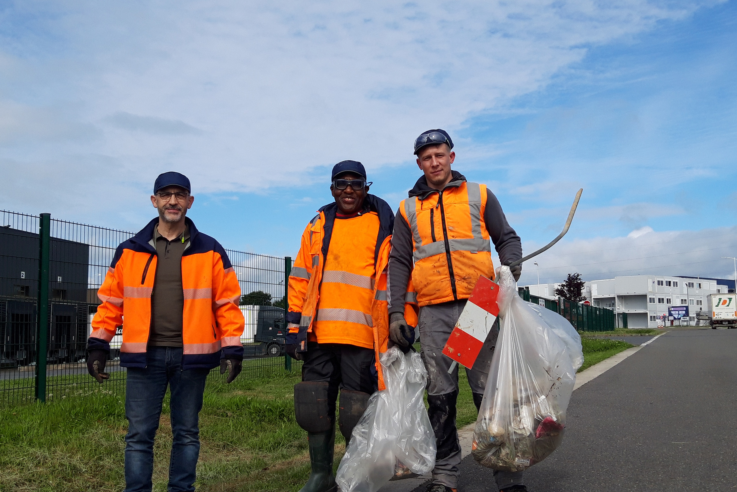 personnes portant des gilets de sécurité orange vif et des gants, en train de ramasser des déchets le long d'une route