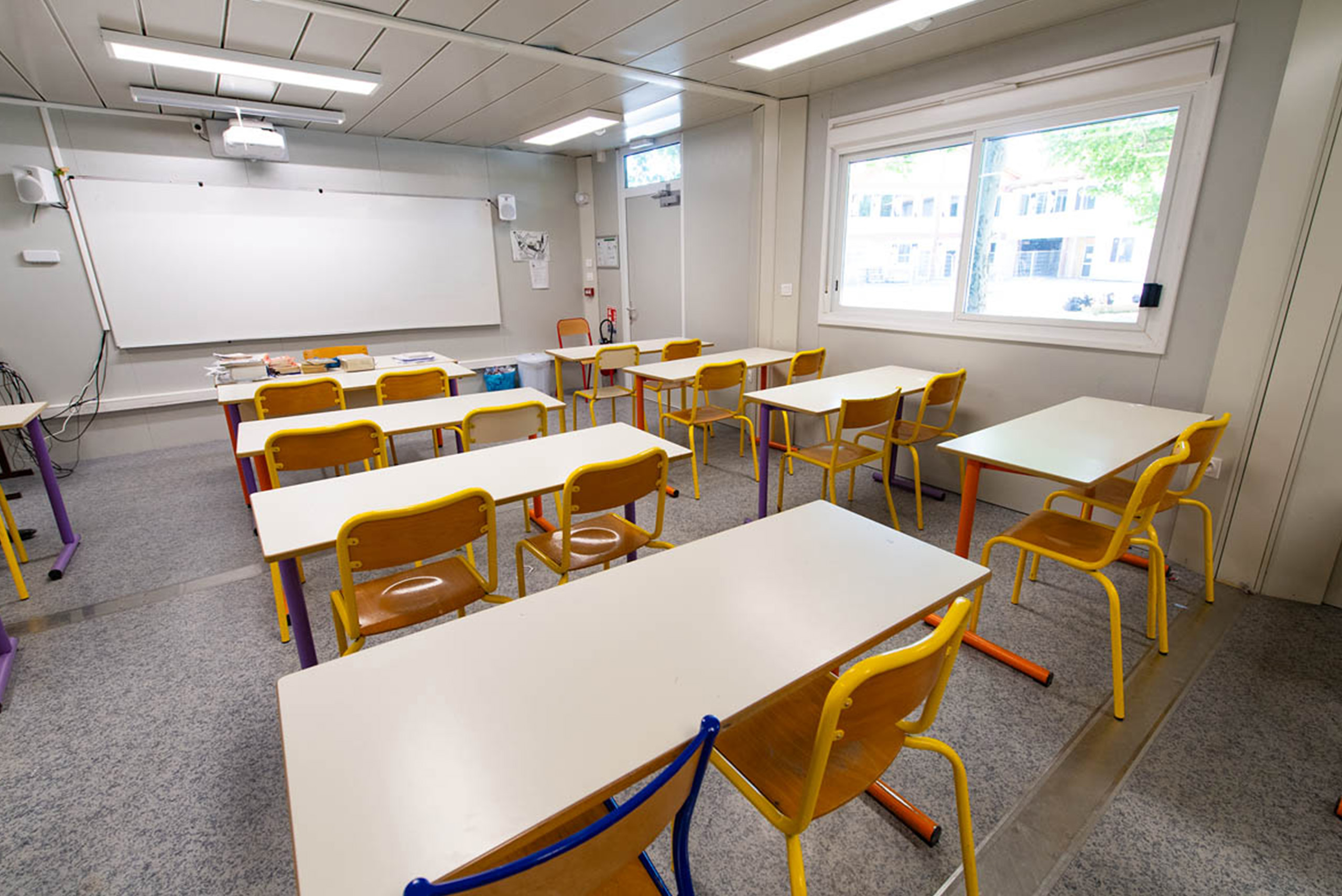 Salle de classe modulaire ALGECO® lumineuse avec tableau blanc et vue sur la cour extérieure