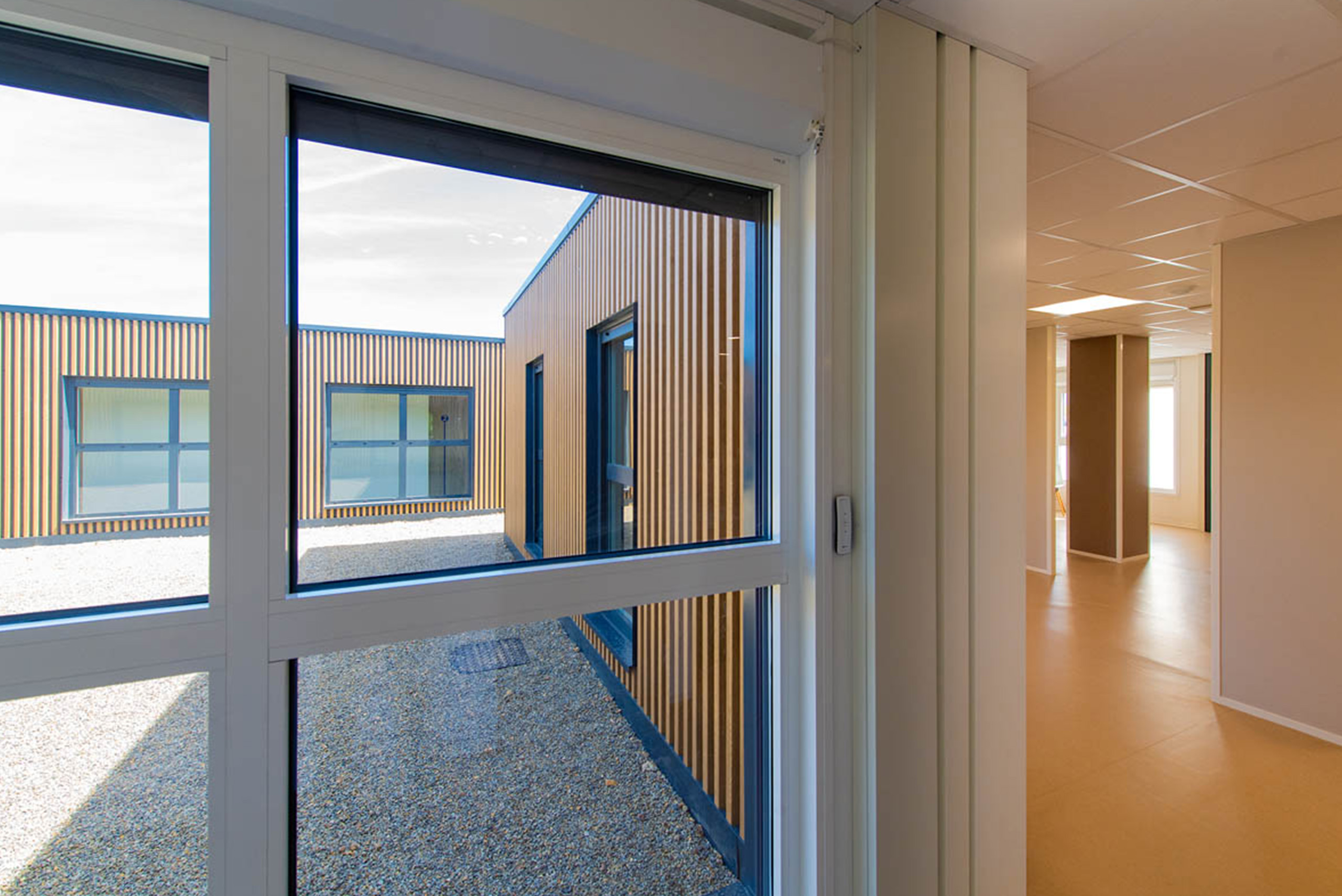 vue intérieure et extérieure de bâtiments modulaires avec bardage bois et métal, couloir blanc et beige