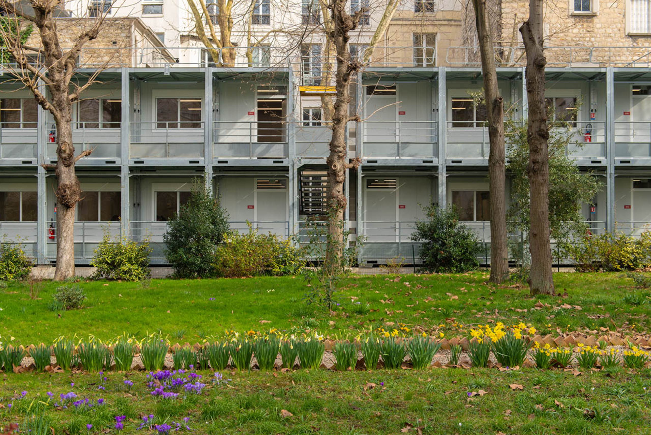 Façade du bâtiment modulaire ALGECO® à deux niveaux, intégrée au jardin fleuri de l’Institut catholique de Paris
