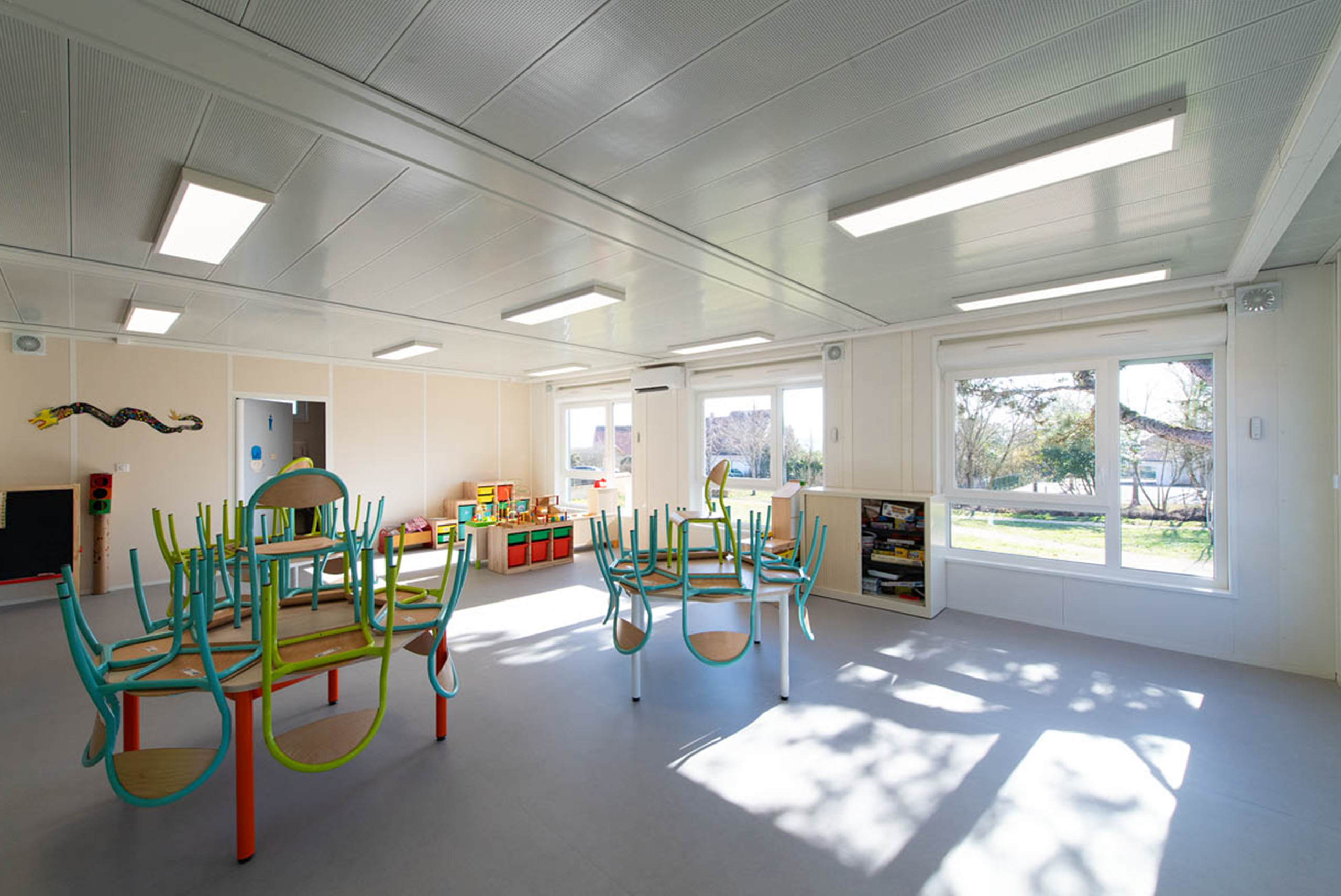 Salle lumineuse de bâtiment périscolaire modulaire ALGECO® avec mobilier scolaire et vue sur l’extérieur