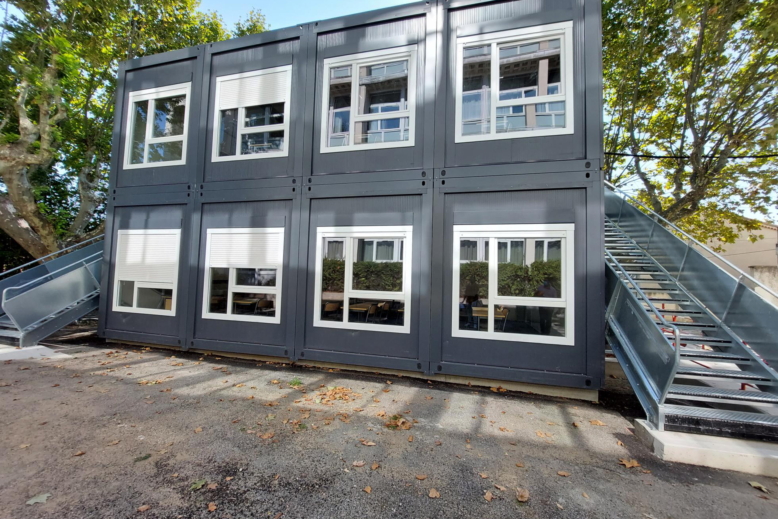 Bâtiment modulaire ALGECO® à deux étages avec escaliers latéraux implanté sous des platanes