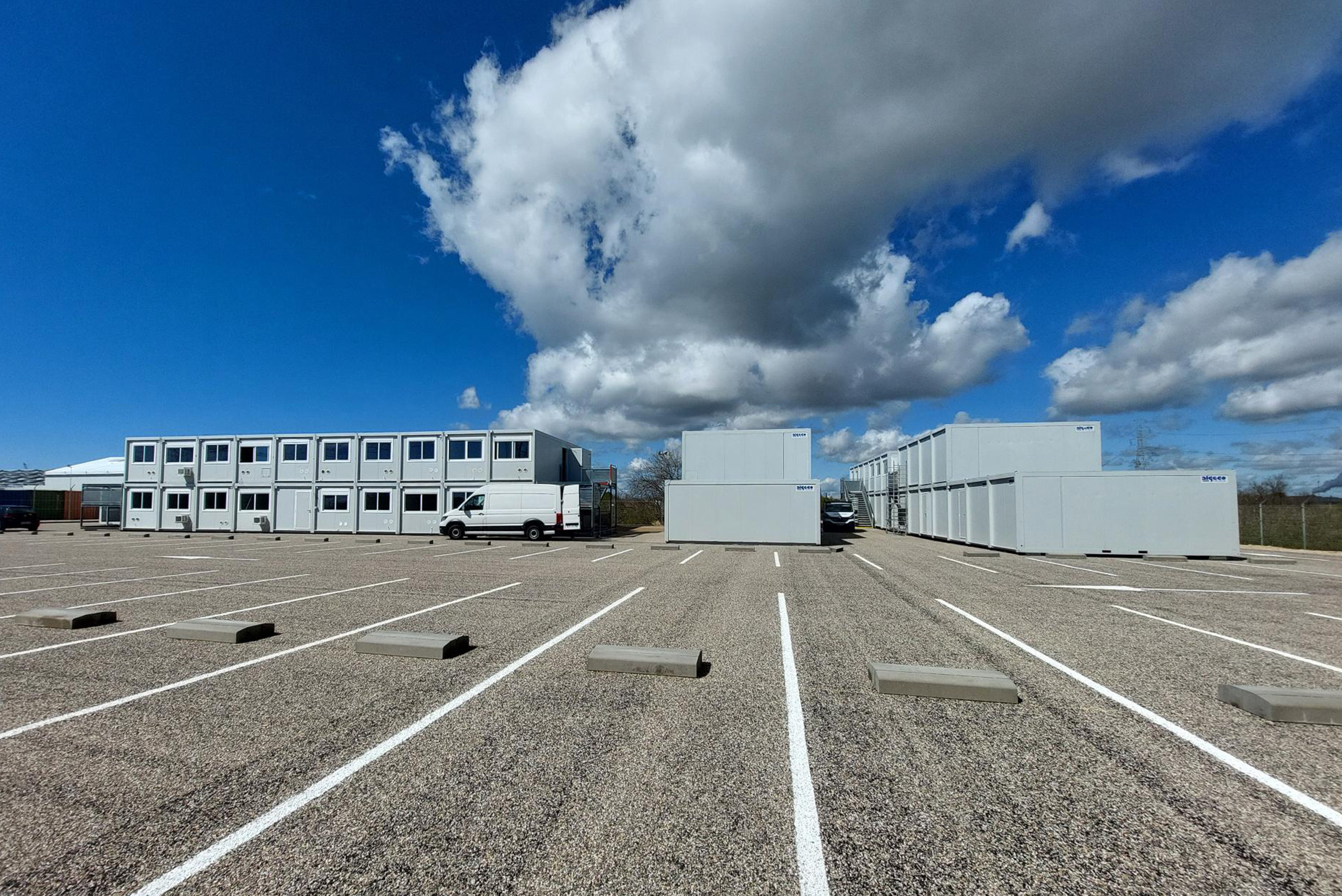 Ensemble de bâtiments modulaires ALGECO® installés sur un parking avec ciel dégagé et nuages