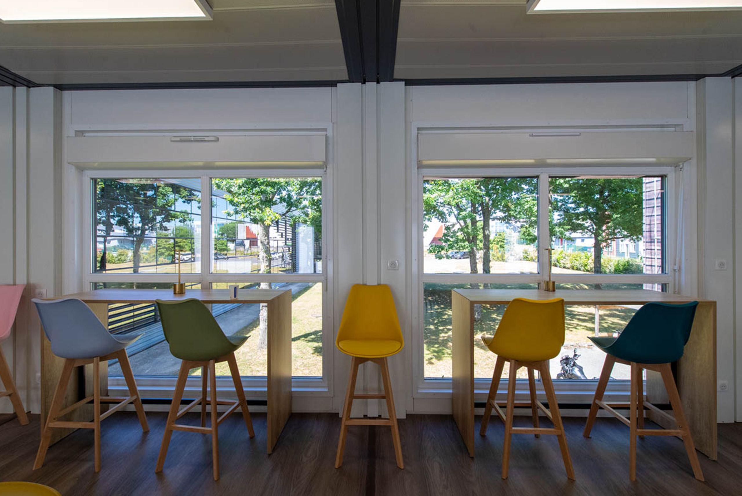 Tables hautes et baies vitrées dans la cafétéria modulaire ALGECO® temporaire de L-Acoustics avec vue arborée