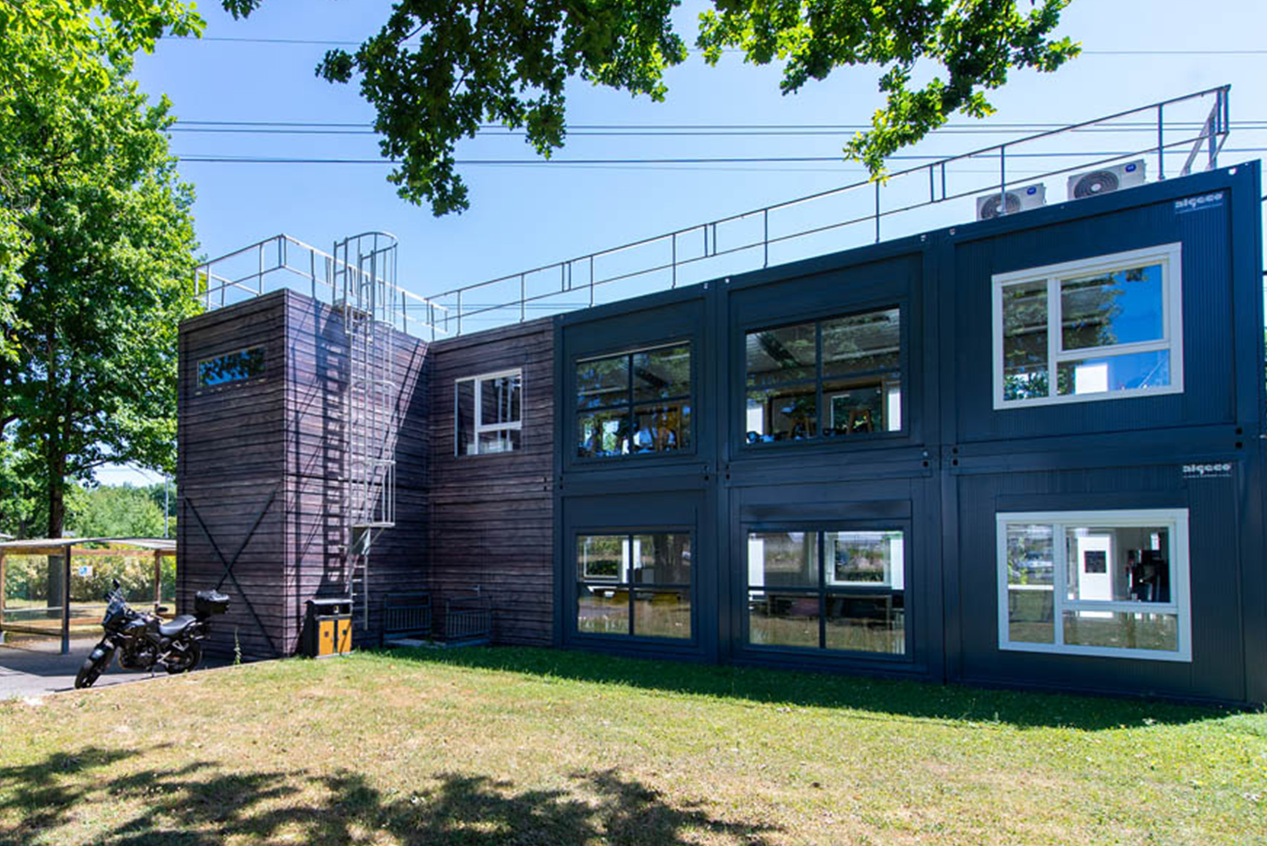 Vue d’ensemble du bâtiment modulaire ALGECO® temporaire de L-Acoustics en R+1 avec bardage bois et parking deux-roues