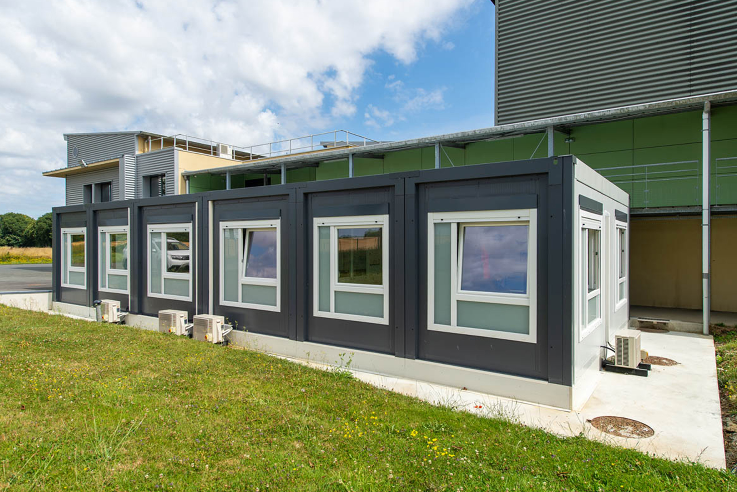 Façade du bâtiment modulaire ALGECO® de bureaux neufs installés sur le site industriel Trinoval Passage couvert entre le bâtiment modulaire ALGECO® et l’usine de Trinoval