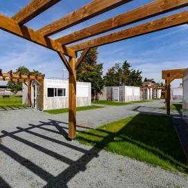 Allée paysagère au sein du village modulaire ALGECO® avec pergolas bois et studios indépendants pour demandeurs d’asile à Villenave-d’Ornon