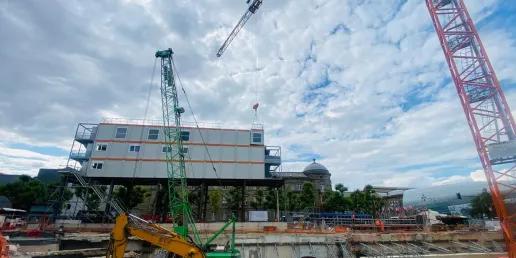 Bâtiment modulaire ALGECO® sur pilotis installé au-dessus d’un chantier urbain avec grues et engins de terrassement