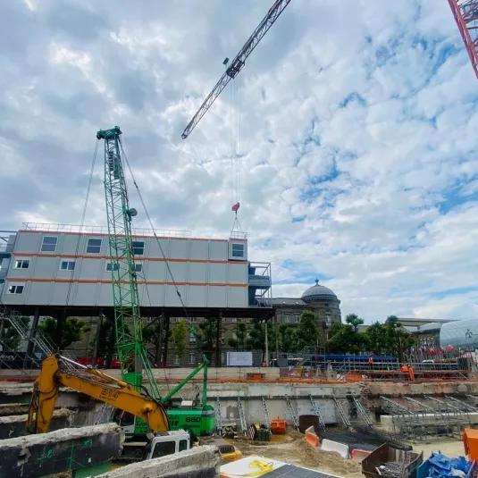 Bâtiment modulaire ALGECO® sur pilotis installé au-dessus d’un chantier urbain avec grues et engins de terrassement