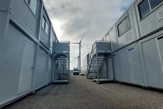 Allée entre bâtiments modulaires ALGECO® à deux niveaux avec escaliers extérieurs et éolienne en arrière-plan