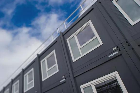 bâtiment modulaire moderne gris foncé avec fenêtres blanches sous un ciel bleu avec quelques nuages
