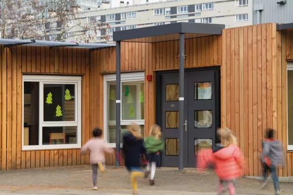 enfants courant vers l’entrée d’une école modulaire ALGECO® avec bardage bois et fenêtres décorées