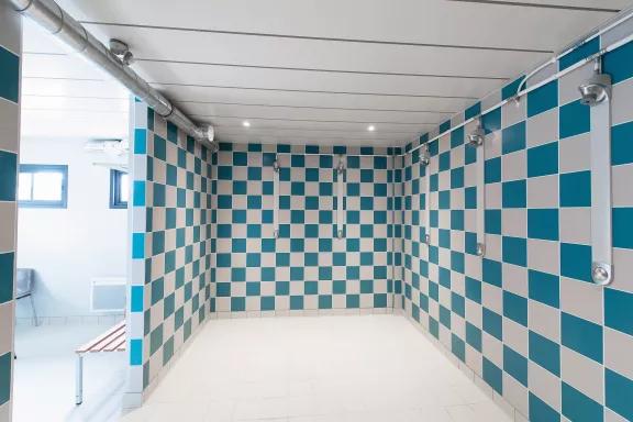 Douche collective avec carrelage mural bleu et gris dans un vestiaire sportif modulaire ALGECO® de Servon