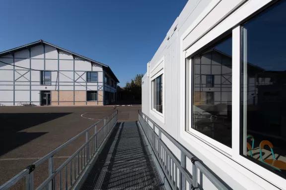 Rampe d’accès PMR vers salle modulaire ALGECO® dans une cour d’école ensoleillée
