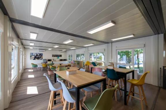 Grande salle de pause d’entreprise modulaire ALGECO® lumineuse avec chaises colorées et tables hautes