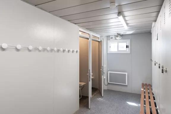 Bloc sanitaire de chantier modulaire avec vestiaires, bancs, patères murales et cabines de douche