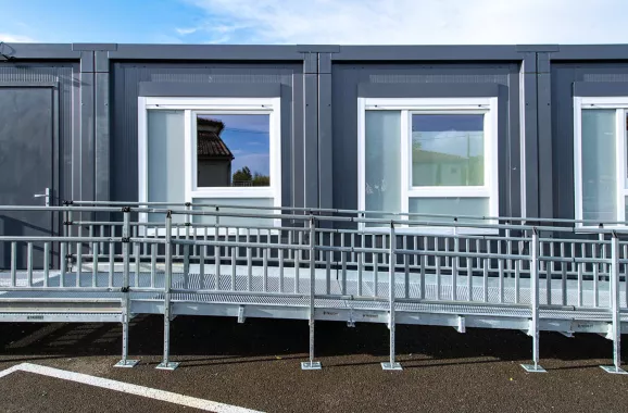 Vue de face de quatre modules ALGECO® alignés en plein air avec fenêtre et rampe d’accès