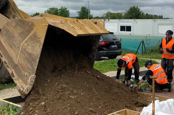 ouvriers d’Algeco en action déversant de la terre grâce à une grande pelle mécanique