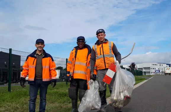 personnes portant des gilets de sécurité orange vif et des gants, en train de ramasser des déchets le long d'une route