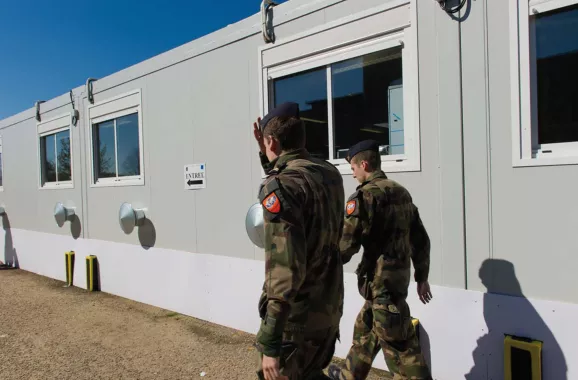 deux militaires en uniforme marchant le long d'un bâtiment modulaire ALGECO®