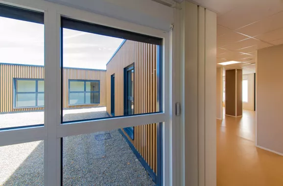 vue intérieure et extérieure de bâtiments modulaires avec bardage bois et métal, couloir blanc et beige