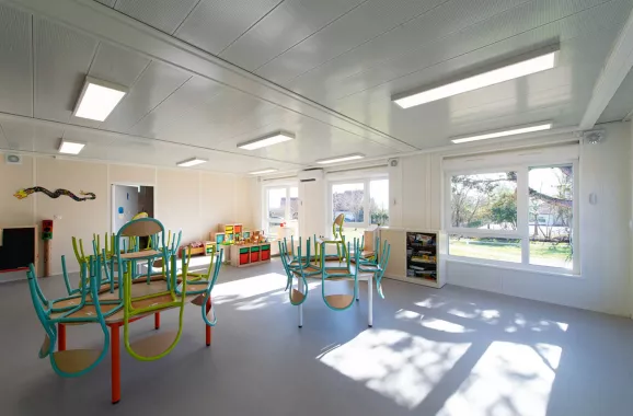 Salle lumineuse de bâtiment périscolaire modulaire ALGECO® avec mobilier scolaire et vue sur l’extérieur