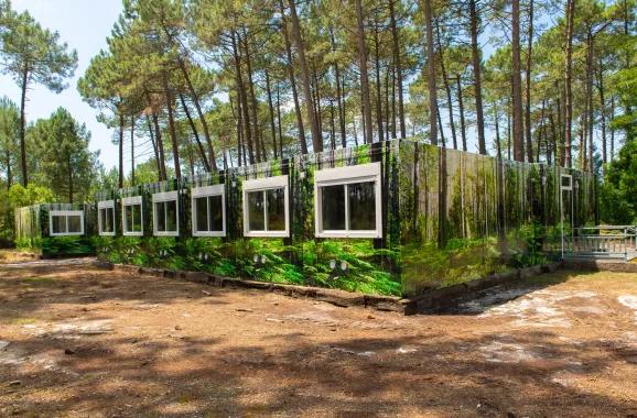 vue dégagée et ensoleillée de la façade en trompe l’œil du complexe de logements modulaires ALGECO® temporaire dans une forêt d’Arès (Bassin d’Arcachon)