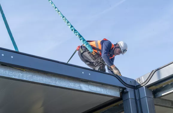 Opérateur en harnais de sécurité travaillant sur l’assemblage d’un module ALGECO® en hauteurLevage d’un module ALGECO® par grue sur un site d’assemblage industriel
