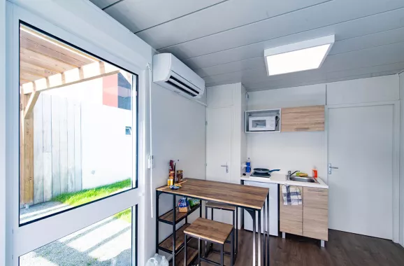 Vue intérieure d’un studio modulaire ALGECO® avec coin repas, kitchenette et baie vitrée donnant sur pergola à Villenave-d’Ornon