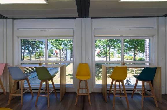 Tables hautes et baies vitrées dans la cafétéria modulaire ALGECO® temporaire de L-Acoustics avec vue arborée