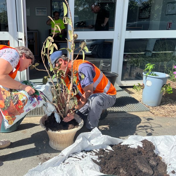 plantage / rempotage d’une plante par deux personnes en gilet de sécurité à l'extérieur d'un bâtiment ALGECO®