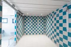 Douche collective avec carrelage mural bleu et gris dans un vestiaire sportif modulaire ALGECO® de Servon