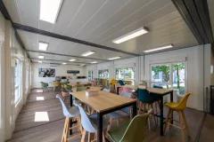 Grande salle de pause d’entreprise modulaire ALGECO® lumineuse avec chaises colorées et tables hautes